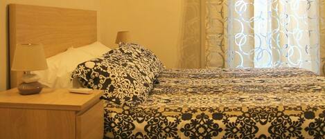 A bedroom with a bed, a nightstand, a lamp, and patterned curtains.