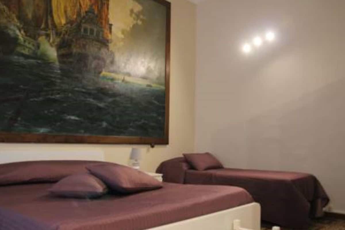 A room with a bed, two bedside tables, and a large painting of a coastal scene.