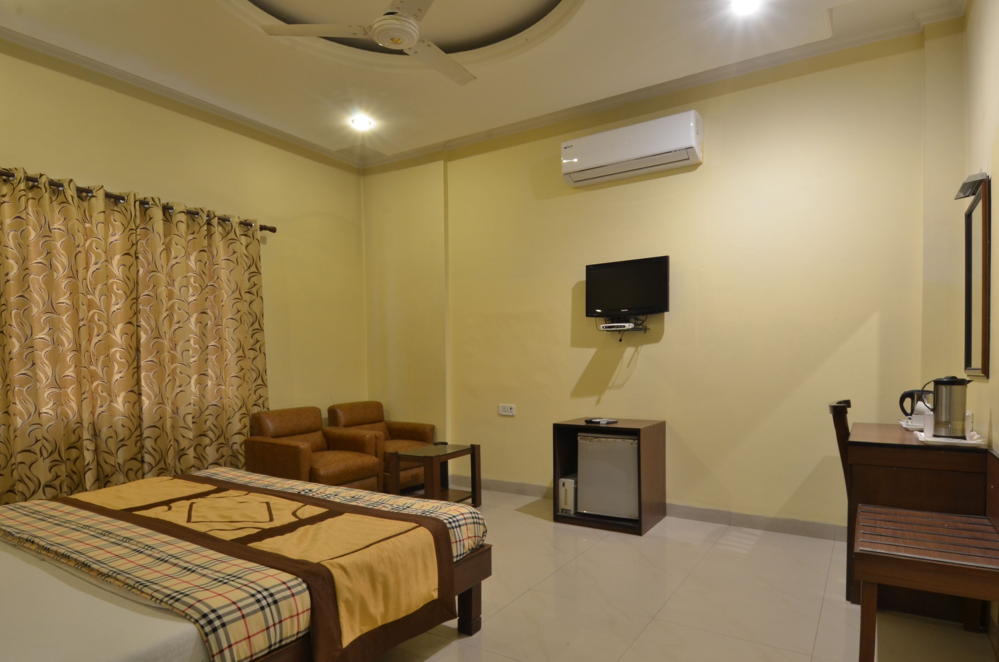 Habitación de hotel con cama, dos sillas, una mesita, televisor, cafetera y aire acondicionado.