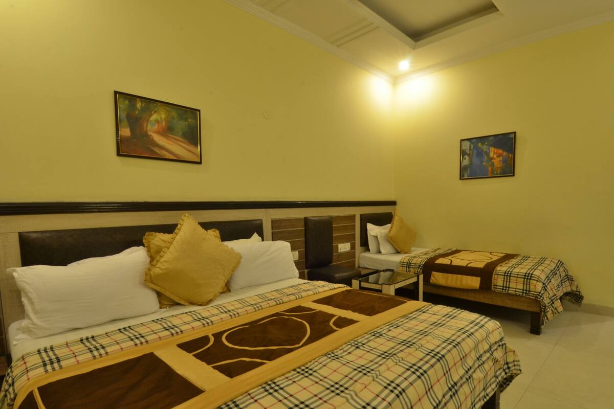 A hotel room with a large bed, two smaller beds, a nightstand, and two paintings on the walls.