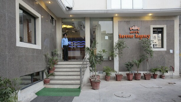 The exterior of Sarovar Regency Hotel with a staircase leading to the entrance, potted plants, and a green mat at the base. - Hotel Sarovar Regency (Amritsar)