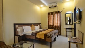 A hotel room with a bed, bedside table, and a small desk with a chair. - Hotel Sarovar Regency (Amritsar)