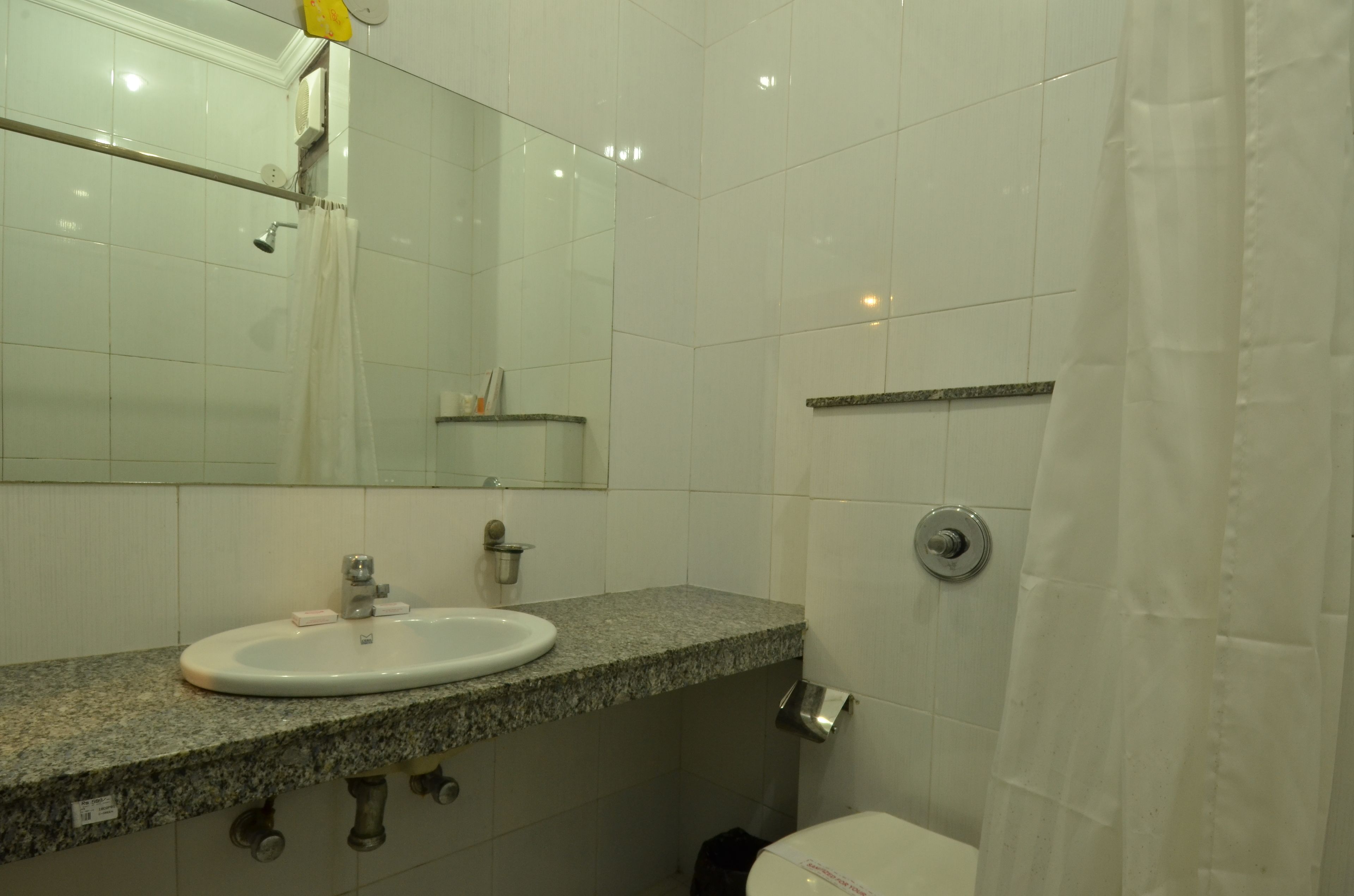 A bathroom with a granite countertop sink, a mirror, a shower curtain, and a toilet.