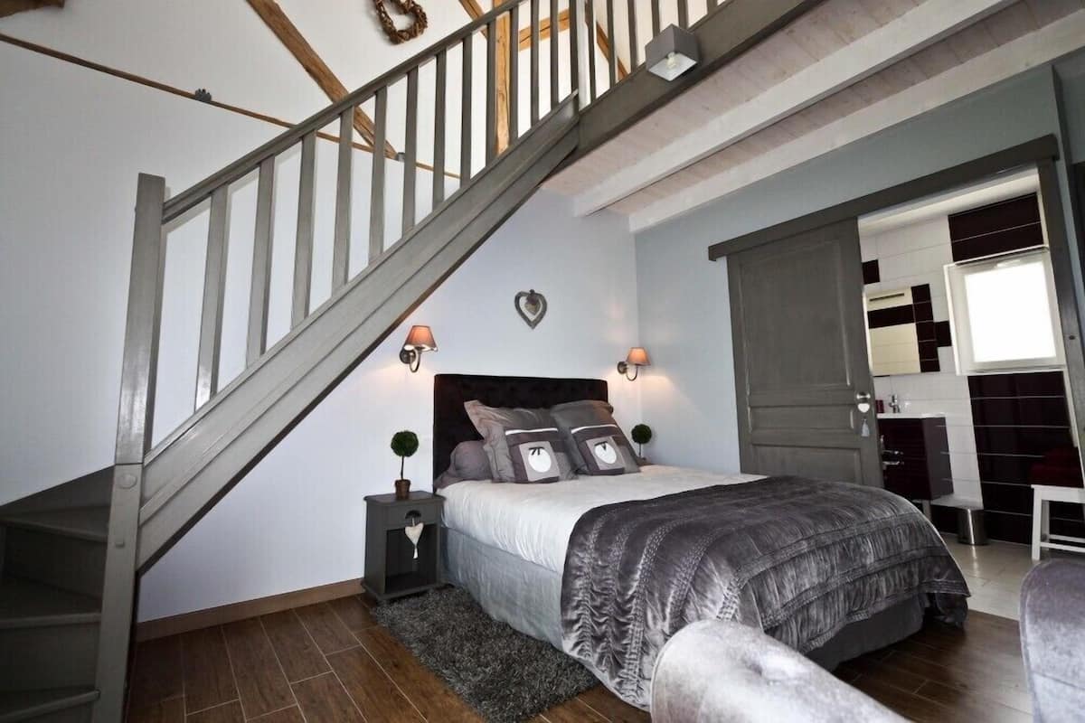A bedroom with a bed, nightstands, a dresser, a mirror, and a staircase.