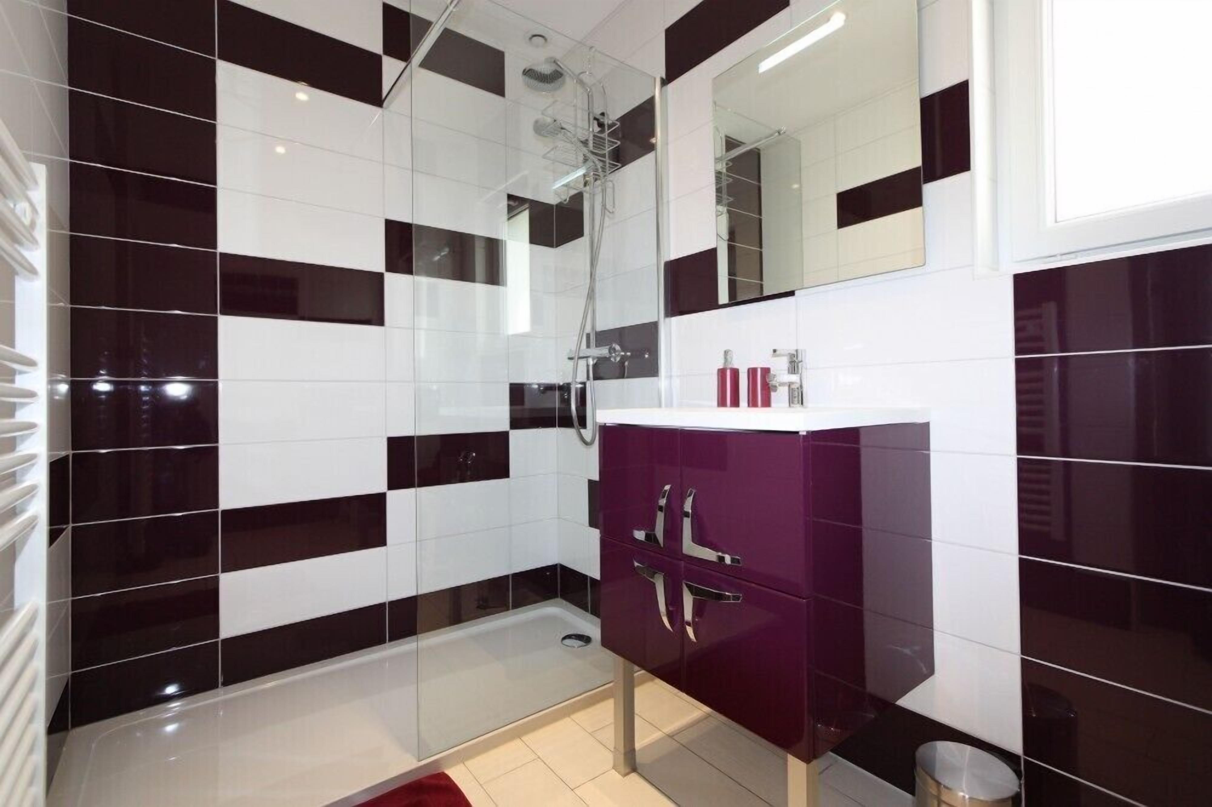 A modern bathroom with black and white tiles, a glass shower enclosure, and a purple vanity.