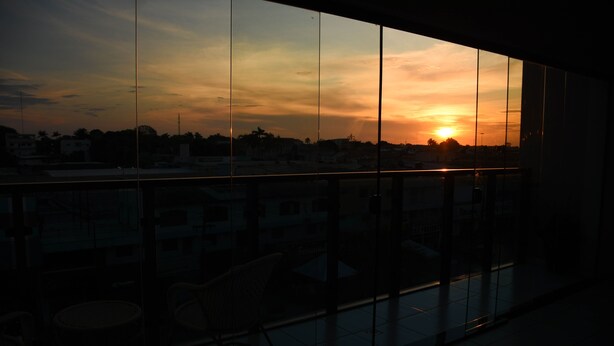 Vista al atardecer a través de una ventana con balcón, sillas y suelo de baldosas.