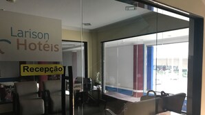 Zona de recepción de un hotel con un panel de vidrio, un mostrador de recepción y un letrero que indica la recepción.