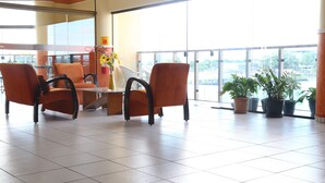 Un vestíbulo amplio con sillones anaranjados, una mesa de vidrio y plantas en macetas.