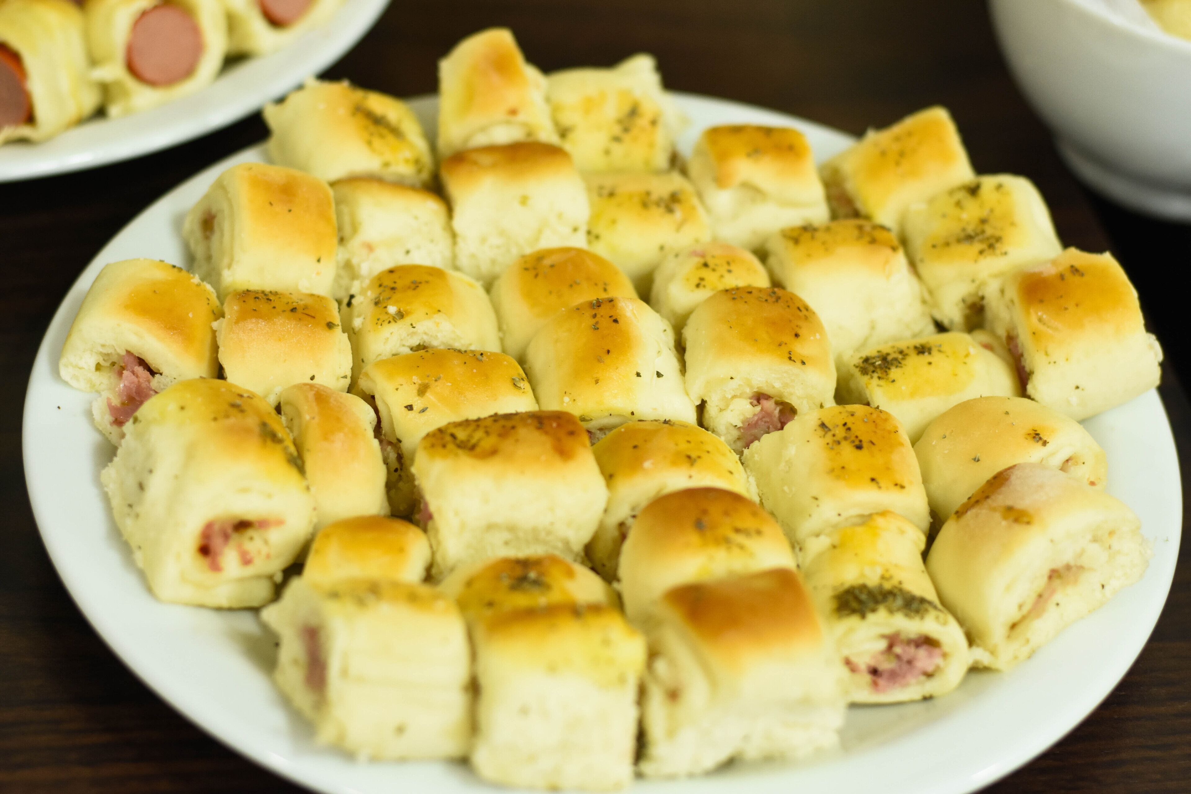 Een bord met kleine, vierkante broodjes met een goudbruine korst, mogelijk gekruid met kruiden, en een zichtbare vulling die vlees zou kunnen zijn.