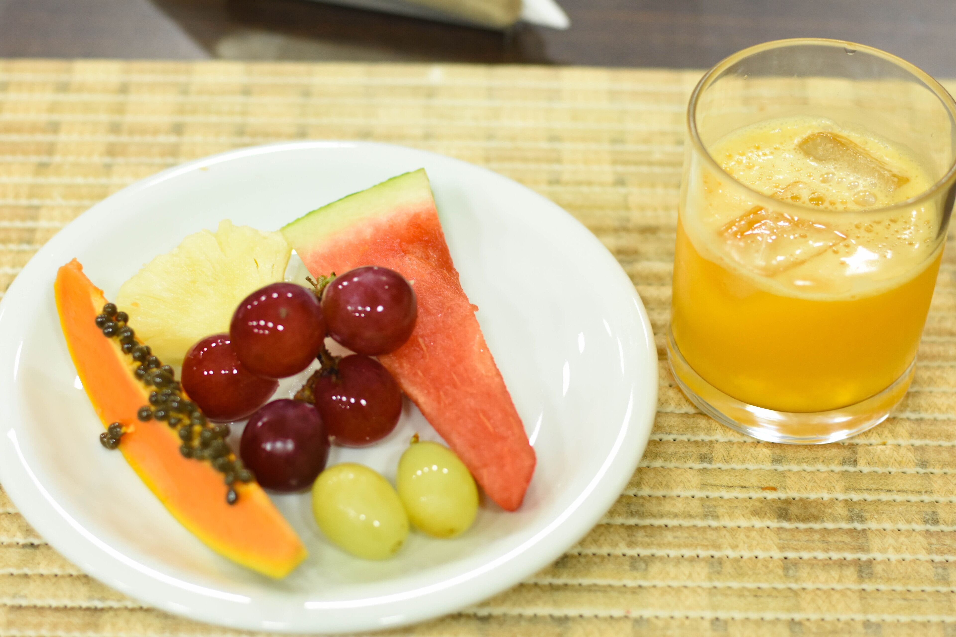 A plate with watermelon, grapes, and papaya, and a glass of orange juice.