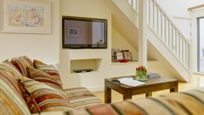 A living room with a sofa, a coffee table with books and a vase, a flat-screen TV mounted on the wall, and a staircase. - Self Catering Holiday Homes Killarney Town Centre (Killarney)