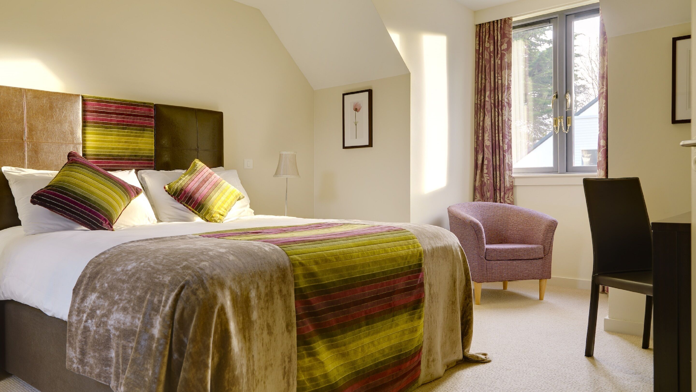 A hotel room with a large bed, a chair, a desk, and a window with curtains.