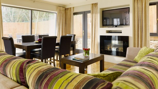 A living room with a sofa, a dining table with chairs, a coffee table, and a TV mounted on the wall. - Self Catering Holiday Homes Killarney Town Centre (Killarney)