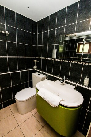 A bathroom with black tiled walls, a green bathtub, a white toilet, and a mirror above the sink. - Balmaha Inn (Drymen)