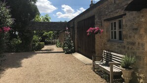 A stone building with a gravel path, a wooden bench, and hanging flower baskets. - Holly House Bed & Breakfast (Chipping Campden)