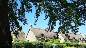 A stone wall with a thatched-roof house in the background. - Holly House Bed & Breakfast (Chipping Campden)