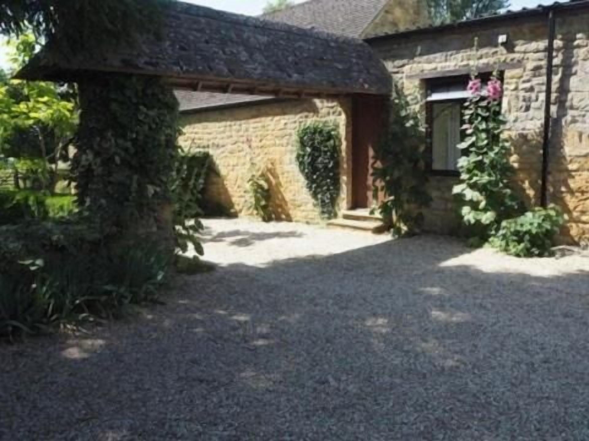 A stone building with a thatched roof, a gravel driveway, and a small garden with climbing plants.
