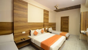 A hotel room with two beds, wooden headboards, a ceiling fan, a wooden door, and a small bedside table with a lamp. - Hotel Metro Jiapur (Jaipur)