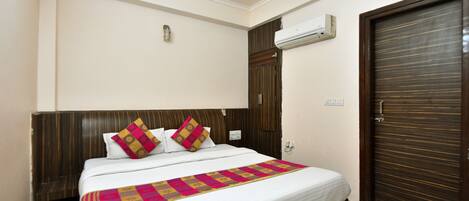 A neatly made bed with a patterned bedspread, a wooden headboard, and an air conditioning unit mounted on the wall.