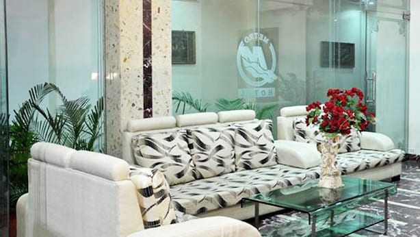 A modern lobby with a glass partition, a white sofa with patterned cushions, and a glass coffee table with a vase of red flowers. - Hotel Metro Jiapur (Jaipur)