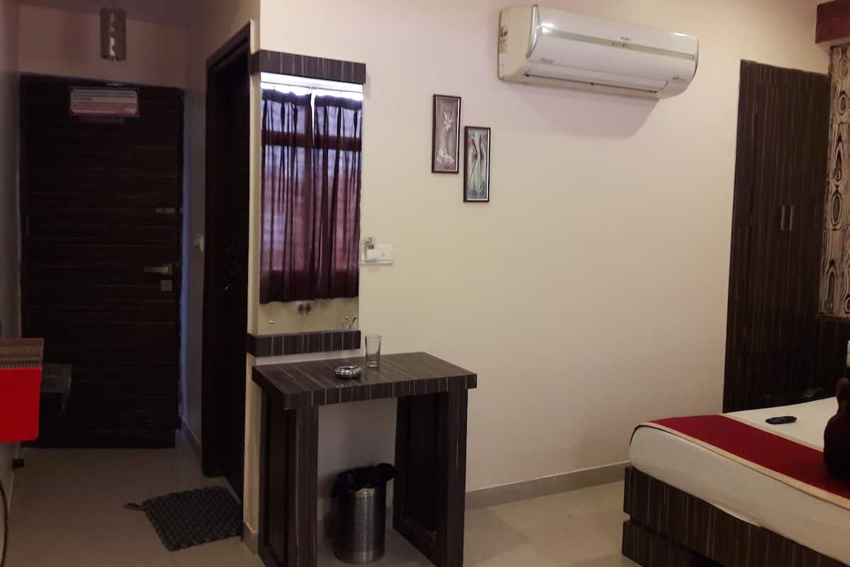 Une chambre d’hôtel avec un lit, une petite table, un miroir, un climatiseur et une porte.