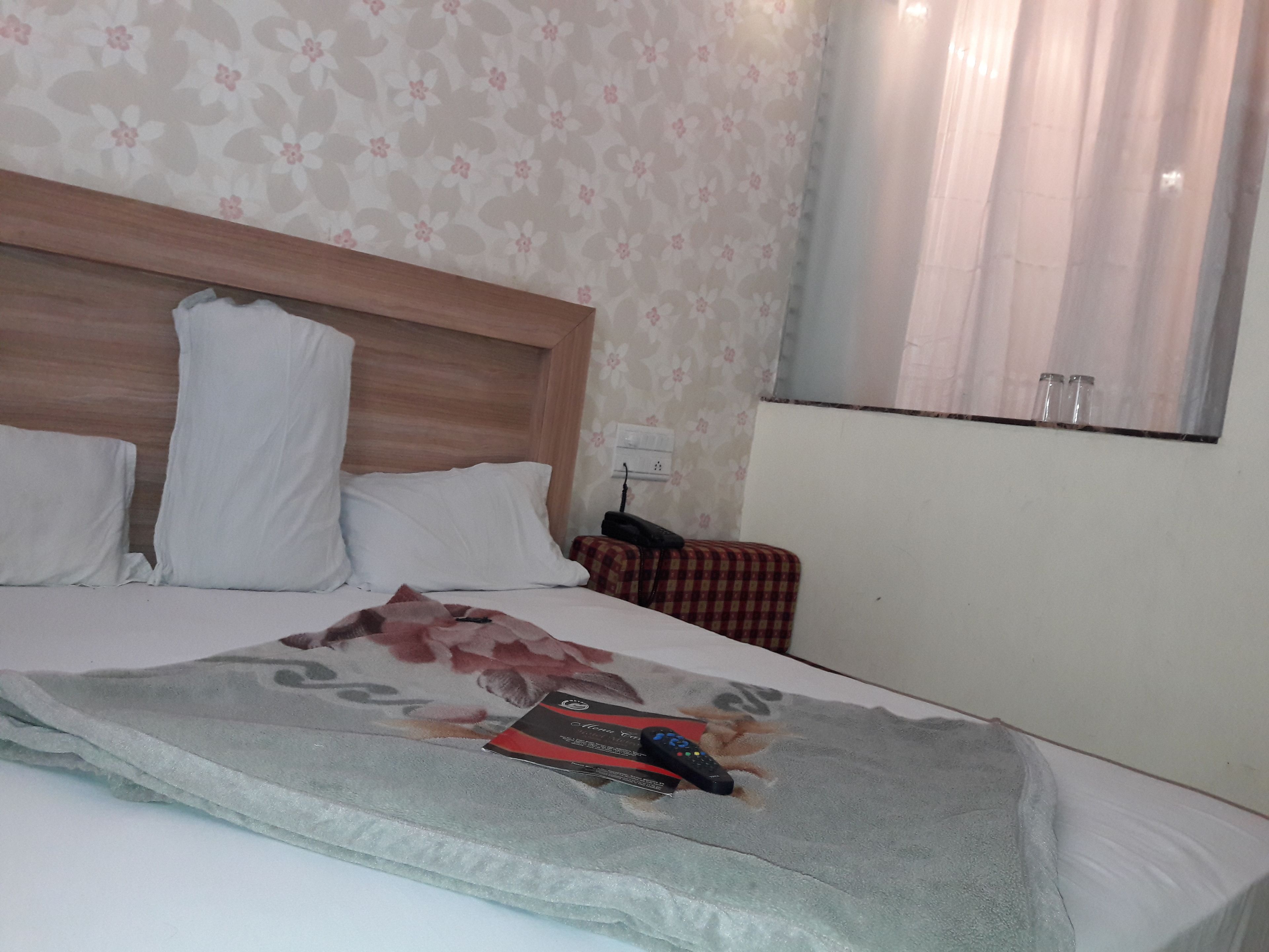 Une chambre d’hôtel avec un lit, une tête de lit, une table de chevet, un miroir et une fenêtre avec des rideaux.