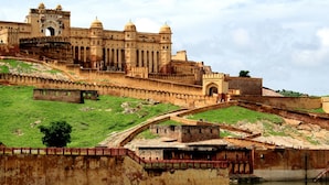 A historic fort with a large central tower, a surrounding wall, and a bridge over a body of water. - Hotel Metro Jiapur (Jaipur)