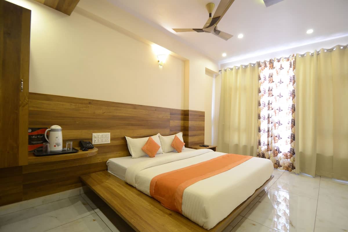 Une chambre d’hôtel avec une tête de lit en bois, un lit avec une literie blanche et orange, une table de chevet avec une machine à café et un ventilateur de plafond.