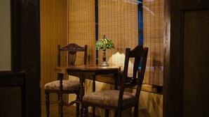 A dining area with a table and two chairs, a table lamp, and a window with blinds. - Gojo Miyabi Inn (Kyoto)