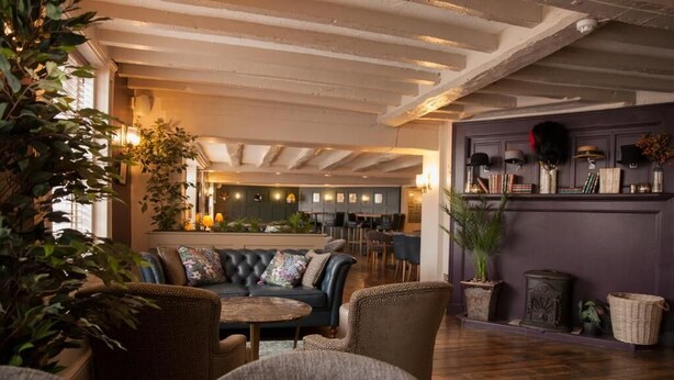 A cozy lounge area with a leather sofa, armchairs, and a coffee table. There is a kitchen area in the background with a bar and seating. - The Falcon Hotel & Restaurant (Bridgnorth)