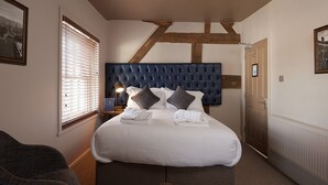 A bedroom with a large bed, a headboard, a window with blinds, a bedside lamp, and a door. - The Falcon Hotel & Restaurant (Bridgnorth)