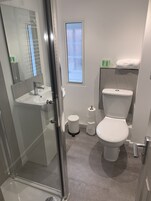 Un baño moderno con cabina de ducha de vidrio, lavamanos blanco, inodoro y una pequeña ventana con vidrio esmerilado.