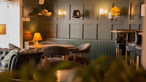 A cozy seating area with leather sofas and chairs, a table with a lamp, and wall-mounted light fixtures. - The Falcon Hotel & Restaurant (Bridgnorth)
