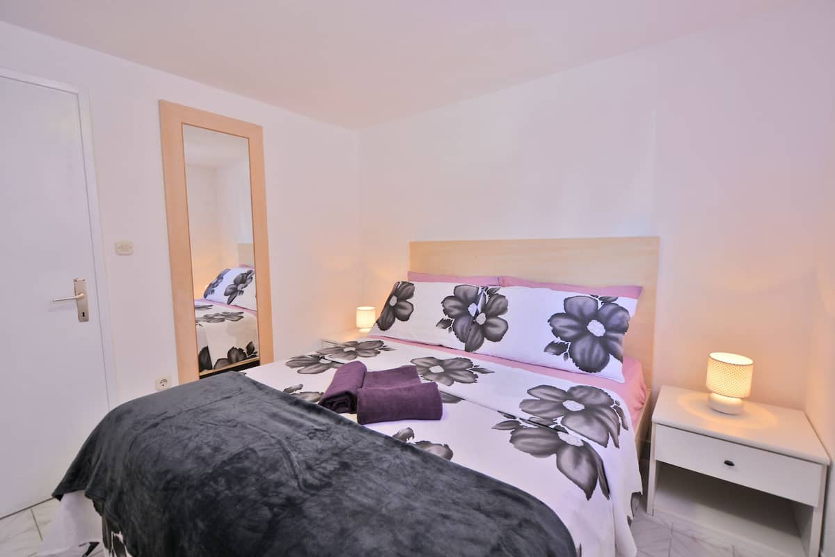 A neatly made bed with floral bedding, a bedside lamp, and a mirror on the wall.