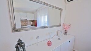Un baño blanco con un espejo grande, un lavabo, un farol decorativo pequeño y un florero con flores rosadas.
