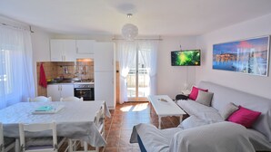 Un espacio habitable compacto con zona de comedor, kitchenette y un sofá con almohadones.