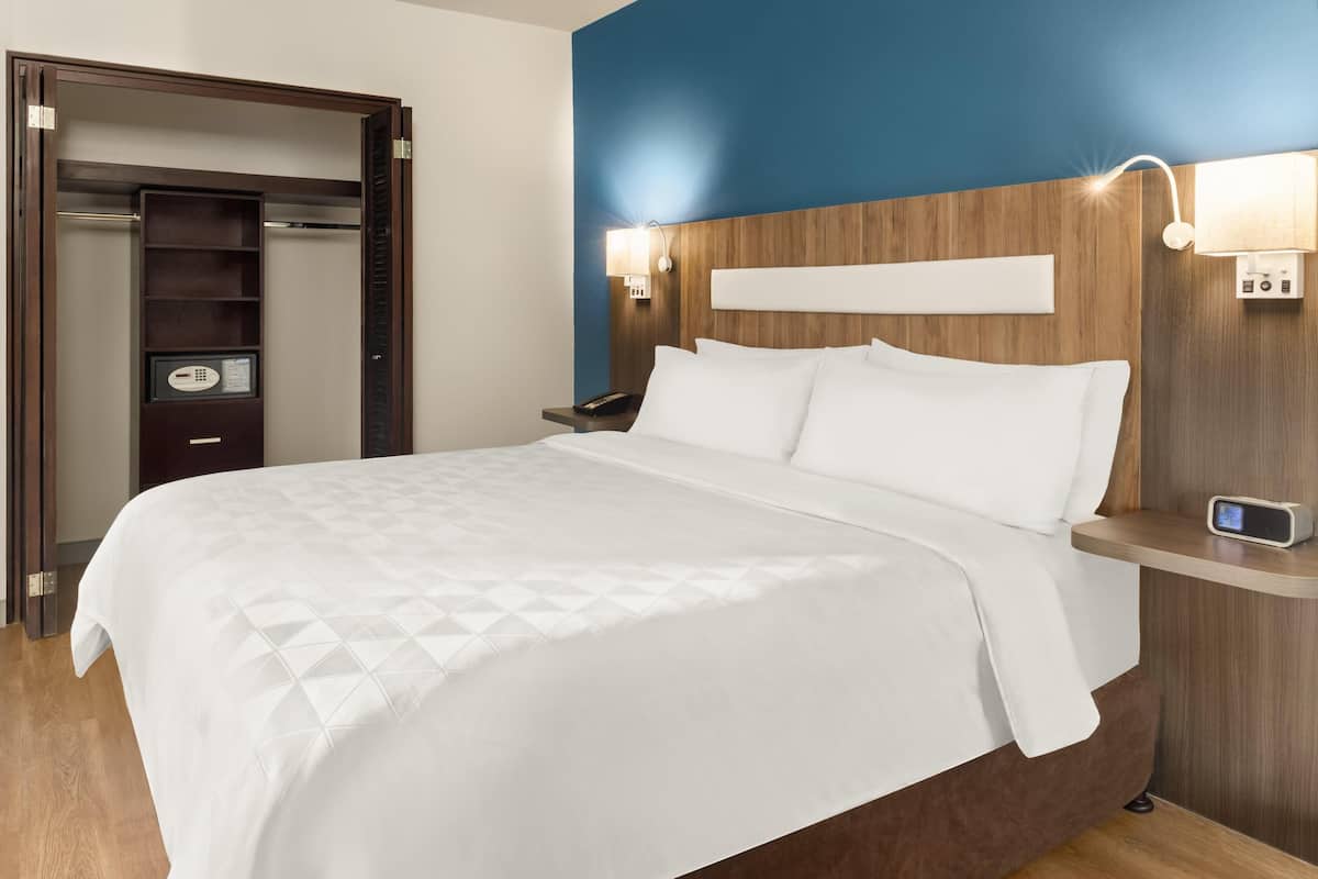 Habitación de hotel con cama, mesita de noche, armario empotrado y lámpara de pared.