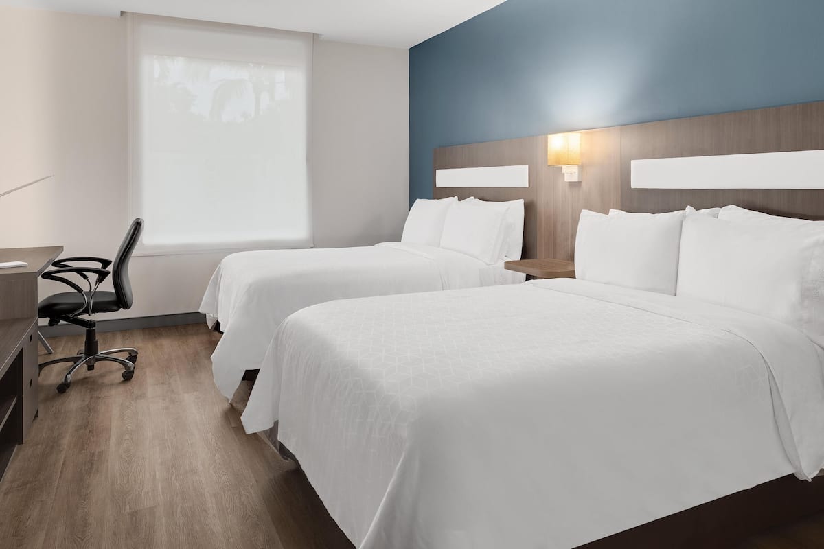 Habitación de hotel con dos camas, un escritorio, una silla y una ventana con persianas.
