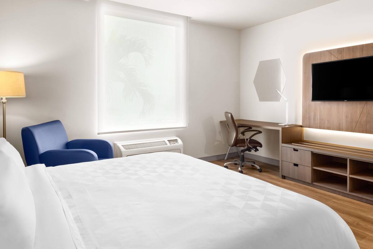 Habitación de hotel con cama, escritorio, silla, televisión y ventana con vistas.