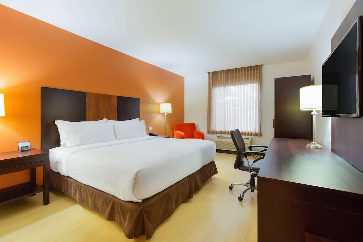 Habitación de hotel con cama, escritorio, silla, televisor y ventana con cortinas.