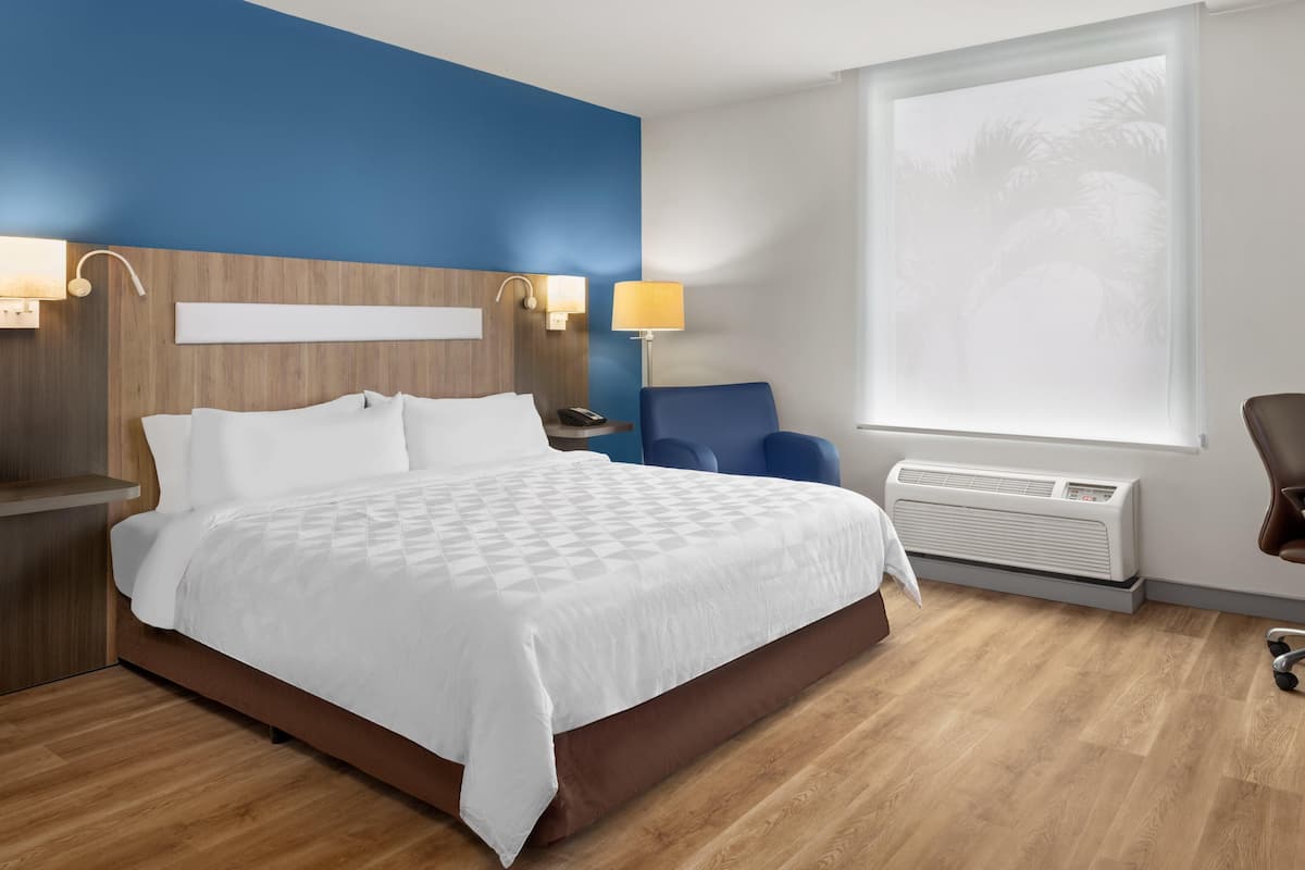 Habitación de hotel con cama, mesitas de noche, escritorio, silla, ventana con vistas y equipo de aire acondicionado.