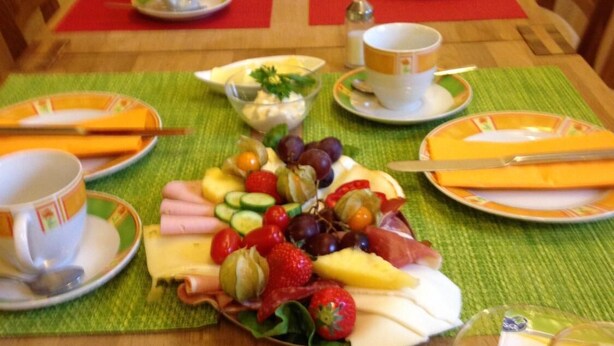 Une table de petit-déjeuner dressée avec des assiettes, des couverts et une variété de fruits et de viennoiseries.