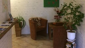 Une petite pièce agréable, avec un sol carrelé, un mur vert orné d’un tableau, un fauteuil marron, une petite table et une plante en pot.
