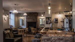 A cozy living room with a fireplace, stone wall, and wooden furniture. There is a bar area with a coffee machine and a large mirror. - The Lion and The Lamb (Seascale)