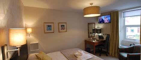Habitación de hotel con cama, escritorio con computadora, silla, televisor y ventana con cortinas.