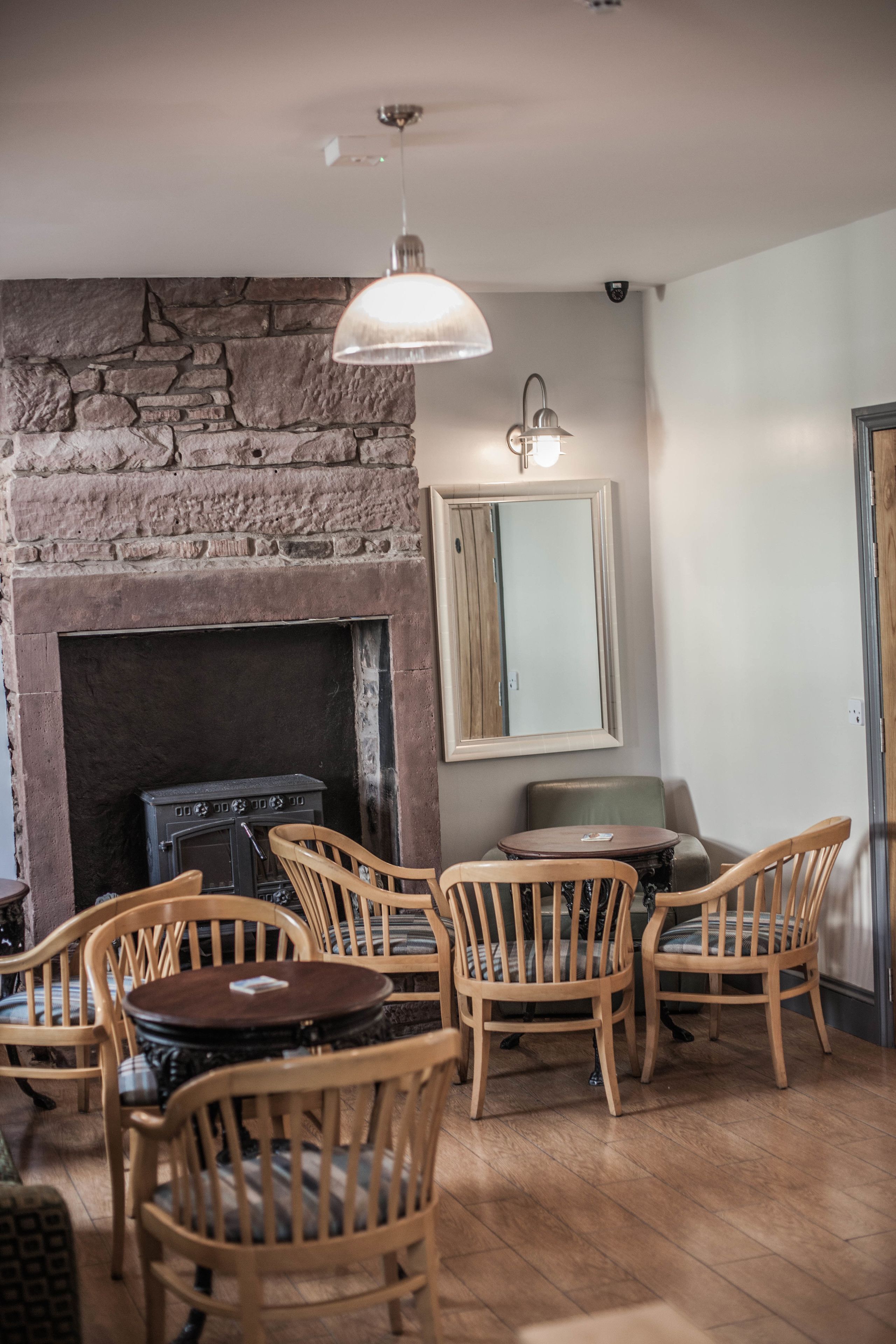 Une pièce chaleureuse avec une cheminée en pierre, des chaises en bois, une table ronde et un luminaire suspendu.