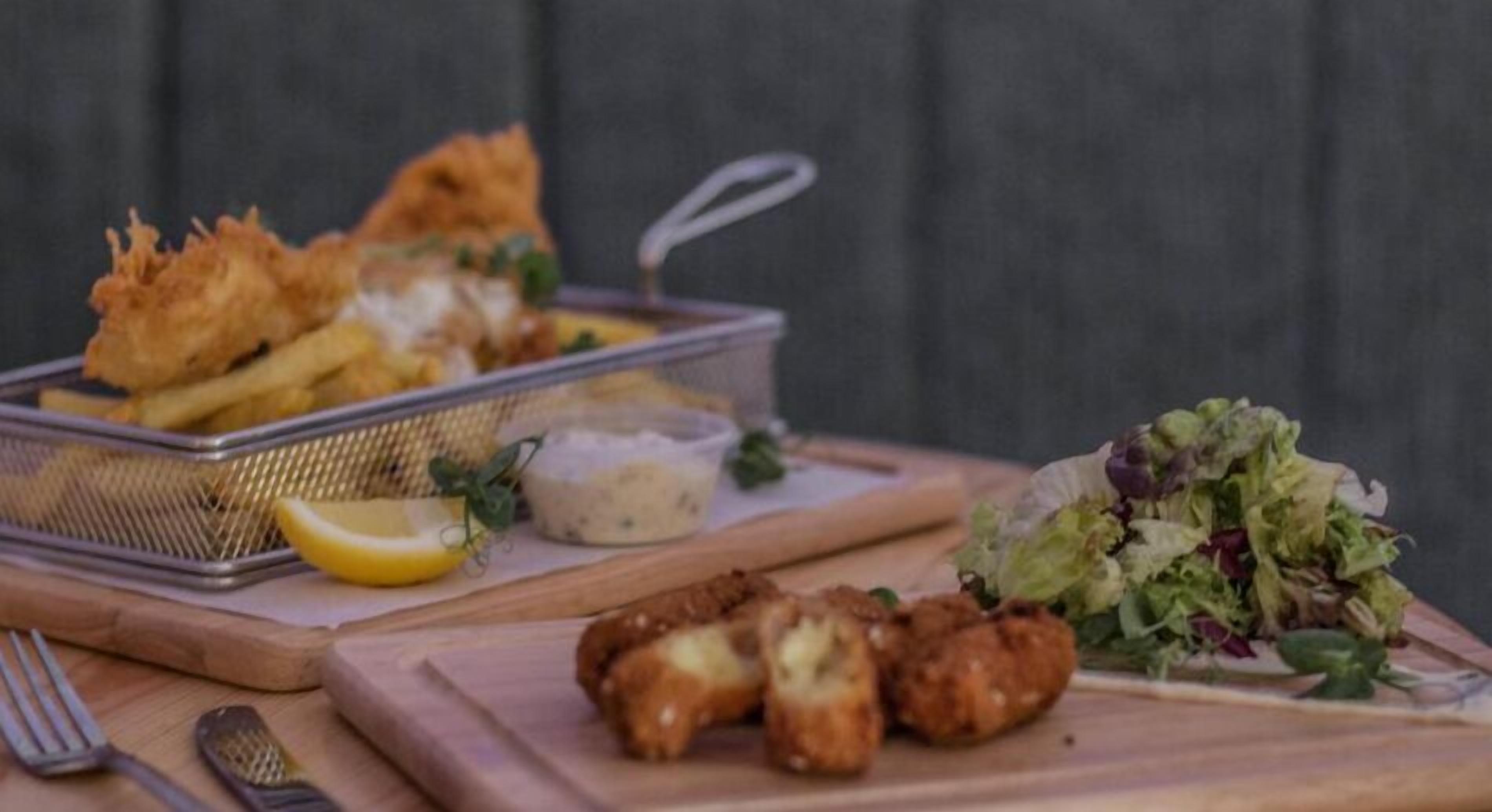 Un plato con pescado frito, papas fritas y una ensalada sobre una tabla de madera.
