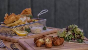 Un plato con pescado frito, papas fritas y una ensalada sobre una tabla de madera.