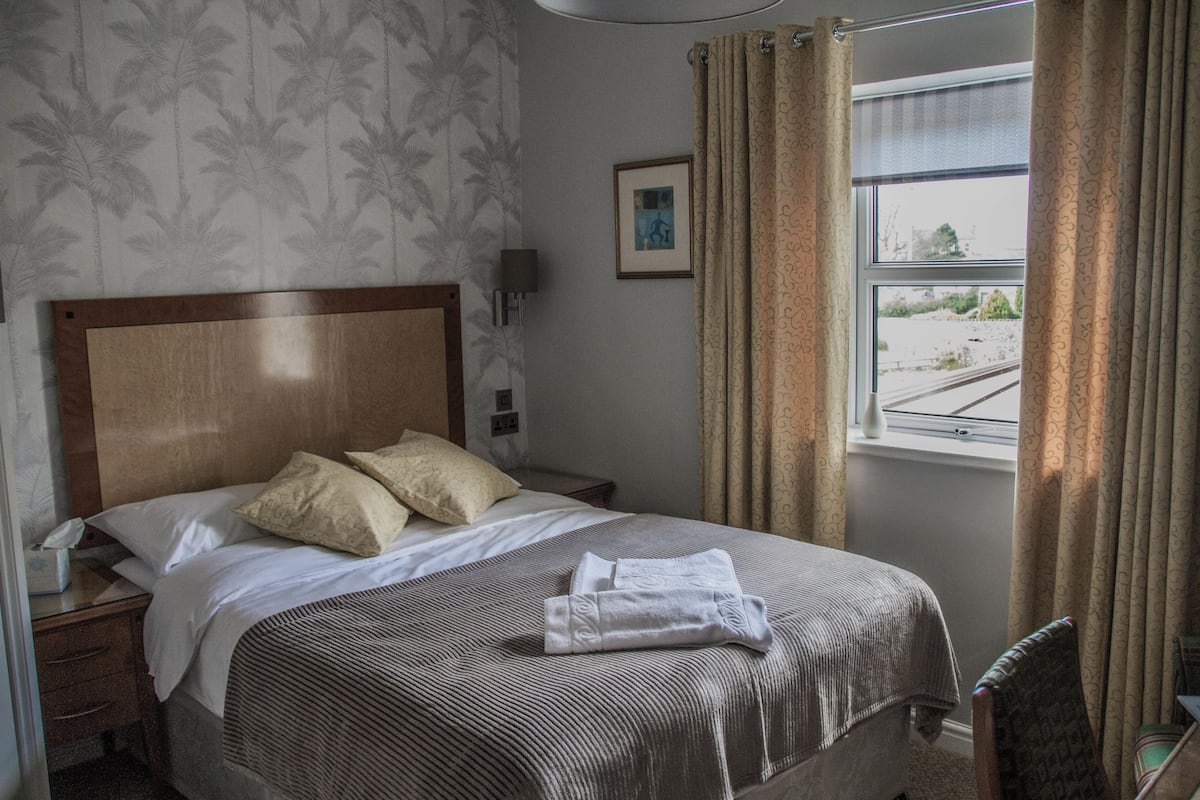 A hotel room with a large bed, a nightstand, a lamp, a framed picture, and a window with curtains.