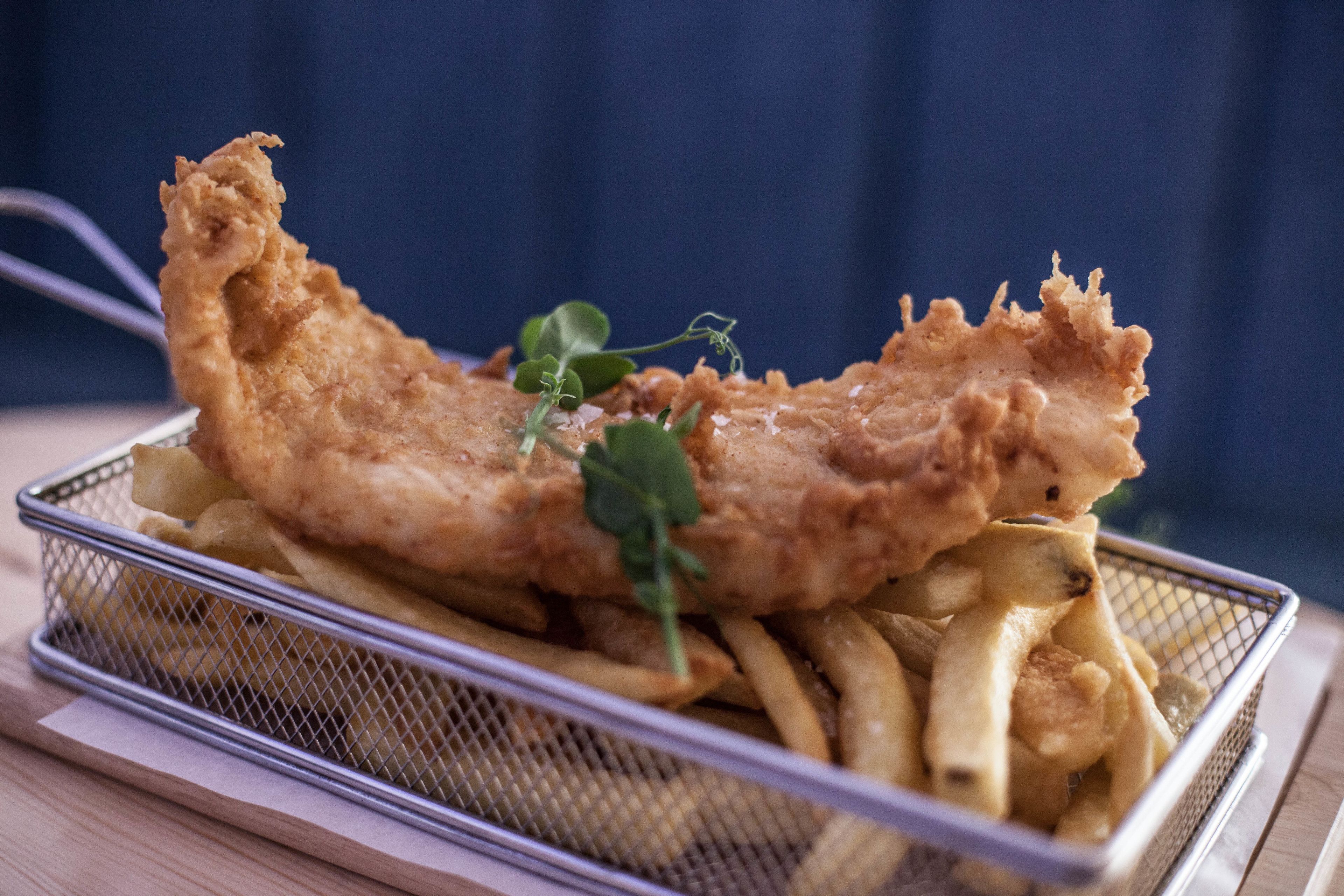Una cesta de pescado con papas fritas y patatas, adornada con hierbas.